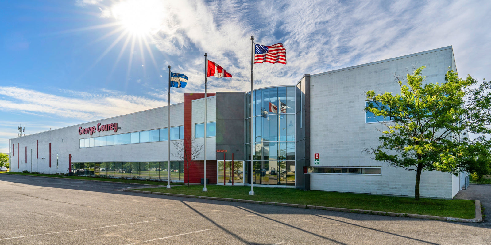 Front view of the George Courey Inc. headquarters in Montreal, featuring a modern building with large glass windows, company signage, and Canadian, Quebec, and American flags under a sunny sky.